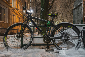 Fototapeta na wymiar snow-covered bike near an apartment building at night during a snowfall