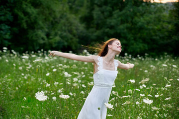 Naklejka na ściany i meble cheerful woman in a field with flowers in a white dress in nature
