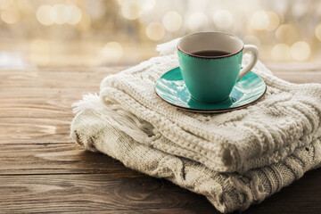 Obraz na płótnie Canvas A cup of coffee on a stack of cozy knitted scarves in pastel colors on a wooden background. Morning cozy coffee. Copy space.