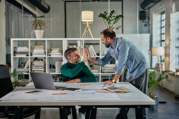 Two male colleagues high-five in office