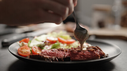 man pour pepper or nut sauce on slices of new york steak on plate with mixed vegetables