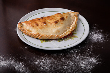 Closed calzone pizza on a white dish on a dark background