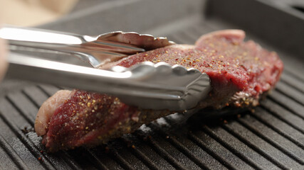 flip new york steak with tongs on grill pan