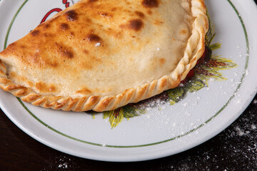 Closed calzone pizza on a white dish on a dark background