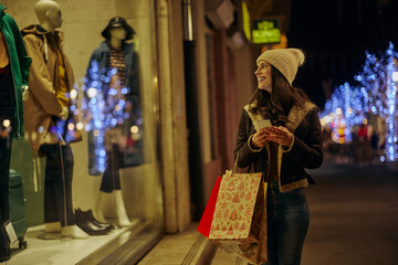 Woman at Christmas shopping using phone and looking in the shop window