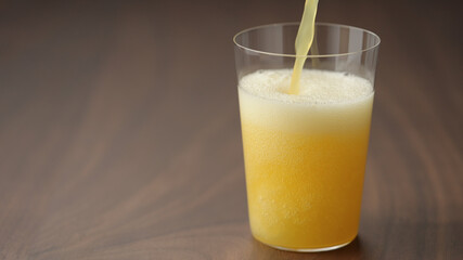 pour yellow drink in tumbler glass closeup