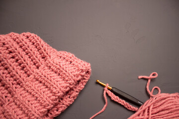 warm hat, yarn crochet and two skeins of pink thread on a gray background