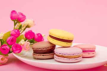 Obraz na płótnie Canvas Plate of macaroons on pink background with flowers. Sweet pastry, baked products, sweets, dessert. Unhealthy diet, sugar dependence.