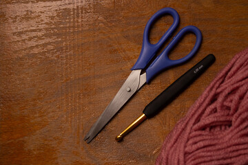 pink yarn with crochet hook and scissors on wooden background