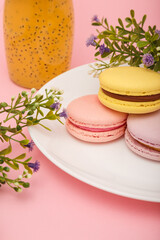 Fototapeta na wymiar Plate of macaroons on pink background with flowers. Drink in bottle. Sweet pastry, baked products, sweets, dessert.
