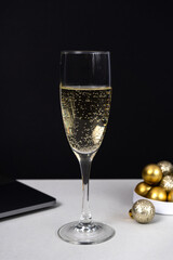 Glass of champagne, Christmas balls and laptop on dark background, celebration and work. Vertical photo