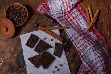 Broken bar of dark bitter chocolate with chilly pepper, cinnamon, red pea pepper inside on paper,...