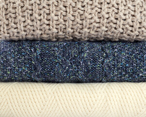 Background from warm knitted sweaters. A stack of blue, beige and white sweaters close up. Stylish clothes for the cold season