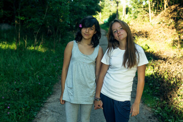Two teenage sisters pose holding hands in the park.
