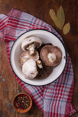 Bowl of fresh raw champignon mushrooms on red kitchen towel, pepper set, bay leaves. Autumn harvest, seasonal jrganic vegan food, healhty eating