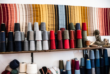 Shelf with colored spools of thread and a rug on the wall.