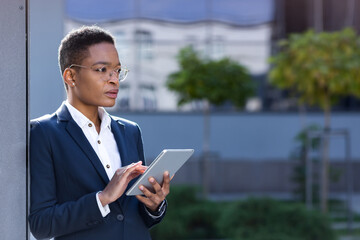 Young successful african american business woman near the office uses a tablet computer, focused and serious online reads