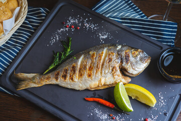 Grilled fish on a plate with a glass of wine and baked vegetables.