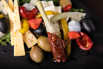 Palette of many types of cheese and some vegetables, tomatoes, paprika, olives.
