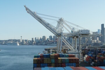 Merchant container ship moored in container SSA terminal to be load and discharged by gantry cranes operated by stevedores. In background skyscrapers of residential area. 