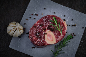 Raw beef shank with garlic, rosemary, salt and pepper. Fresh raw osso buco veal shank on baking paper. top down view. Flatlay of fresh beef cut
