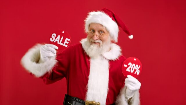 Christmas SALE -20 Off. Cheerful Santa Claus is Dancing and Joyful From Christmas Sale Holding Two Banners With Inscription SALE and -20 Off Showing Off Inscriptions to Camera on Red Background.