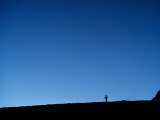 Naklejka na ściany i meble silhouette of photographer that staying with three pod under blue sky on hill