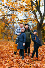 Naklejka na ściany i meble Portrait of a family with children in an autumn city park - happy people posing together near big tree, beautiful nature with yellow leaves as background.
