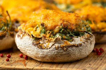 Soft cheese and spinach stuffed mushrooms with cheesy crust served on rustic wooden board, vegetarian food.