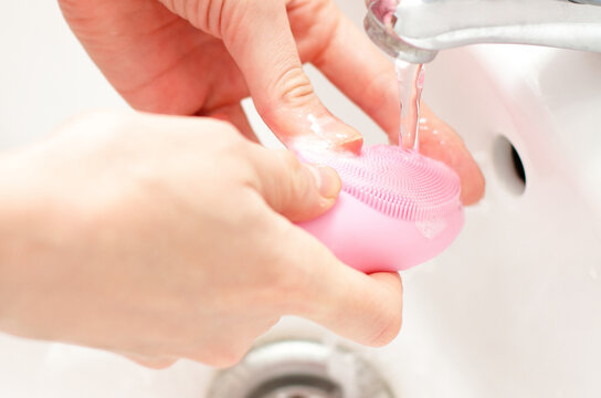 Pink facial sonic brush under faucet water, face skin care treatment
