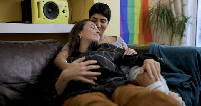Happy girl friends lesbian couple with pregnant woman relaxing on the sofa