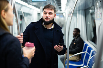 Portrait of young bearded man talking with young woman while traveling by subway