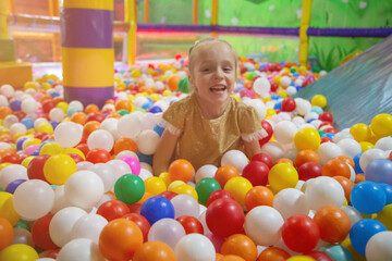 Fototapeta na wymiar Happy laughing girl having fun in ball pit in kids amusement park and indoor play center.