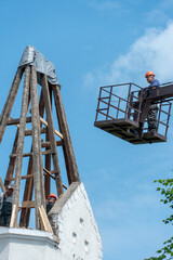 Repair of the old wooden roof of a beautiful historical building. The crane lifts the builders to a height on a special cradle or basket to perform the work. Carpenter on the roof.