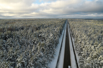Aerial view of asphalt highway leading through frosty winter forests and groves covered with hoarfrost and snow. Drone photo of black road line and trees with chill snow in mountains. Christmas theme