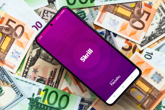 smartphone screen with digital payment service Skrill mobile application on US dollar and euro banknotes background