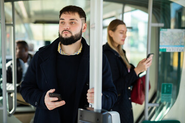 Portrait of focused guy holding on handrails in modern city bus during daily commute to work in autumn day