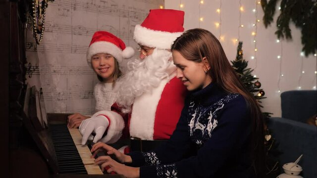 Santa Claus plays with children, girls on the piano. Christmas eve, Christmas tree, family at home. Christmas Eve, kids family holiday concept. Christmas party at home. Children's games with Santa
