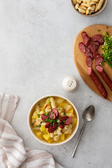 Potato and yellow pea soup with croutons and smoked meats in bowls, cutting board with chopped green onions and smoked sausage, top view