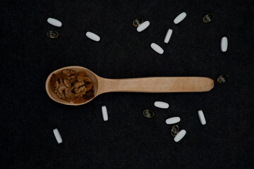 Peeled walnuts and raisins in a wooden spoon. White tablets and capsules. Medical tablets and capsules. Medicines and vitamins. Pharmacology. Healthy Eating. Photo on a dark background.