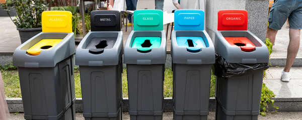 Row of many different multicolored plastic waste cans for garbage sorting and recycling at city street outdoors. Environmental protection and nature cotamination danger prevention concept