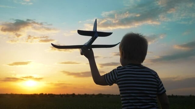 boy kid run in the park across the field play with an toy airplane in his hand a lifestyle silhouette at sunset wants to be an astronaut pilot. dream kid concept. child run on wheat play with toy