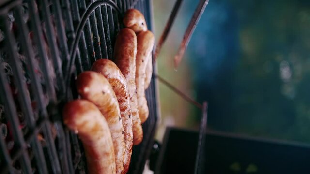 Meat sausages are fried on the grill of the street grill. Cook turns bratwurst over with tongs. Vertical video