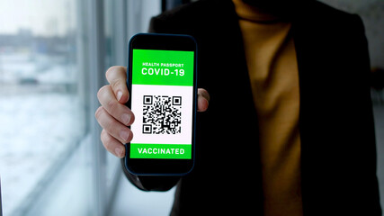 Man points into camera phone with Immune digital passport for covid-19 at airport, shop, cafe. Smartphone with qr code in hand.