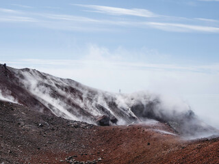 Silhouette of man hiking at coldera of Avachinsky stratovolcano, also known as Avacha Volcano. Backpacker tourist moves upon rocks behind steam from hot geysers. Kamchatka Peninsula, Russia.