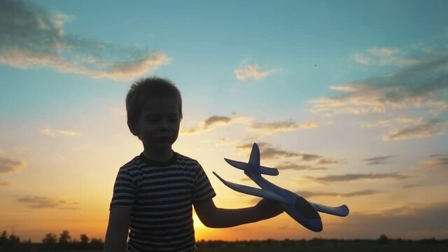 happy boy child go runs with an airplane playing pilot wants to fly. kid silhouette play aircraft. happy family dream freedom concept lifestyle. son runs on a wheat field at sunset holds in his hands