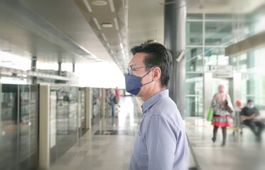 Asian businessman wearing face mask waiting for train on platform. Masked transit concept.
