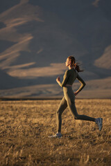 A sportive girl goes jogging against the backdrop of the sunset mountains.