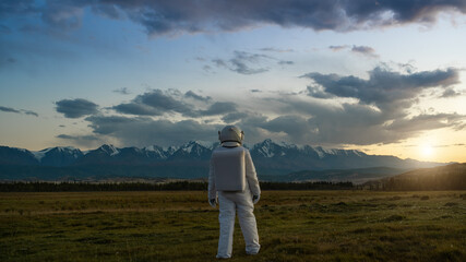 An astronaut explores an unknown planet. Sunset sky and mountains in the background.