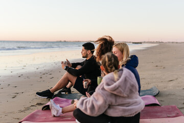 Multiethnic group of people sitting on a beach drinking tea during sunset